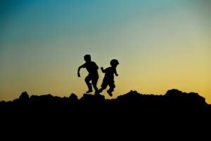 contraluz de dos niños corriendo sobre unas rocas